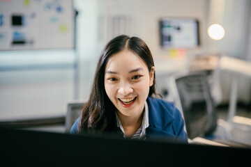 Young businesswoman smiling and working on her computer in a modern office, focused and cheerful