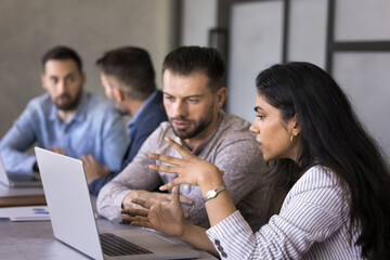 Two focused multiethnic business professional colleagues discussing online project, job application, Internet presentation, working together at laptop, looking at screen, speaking