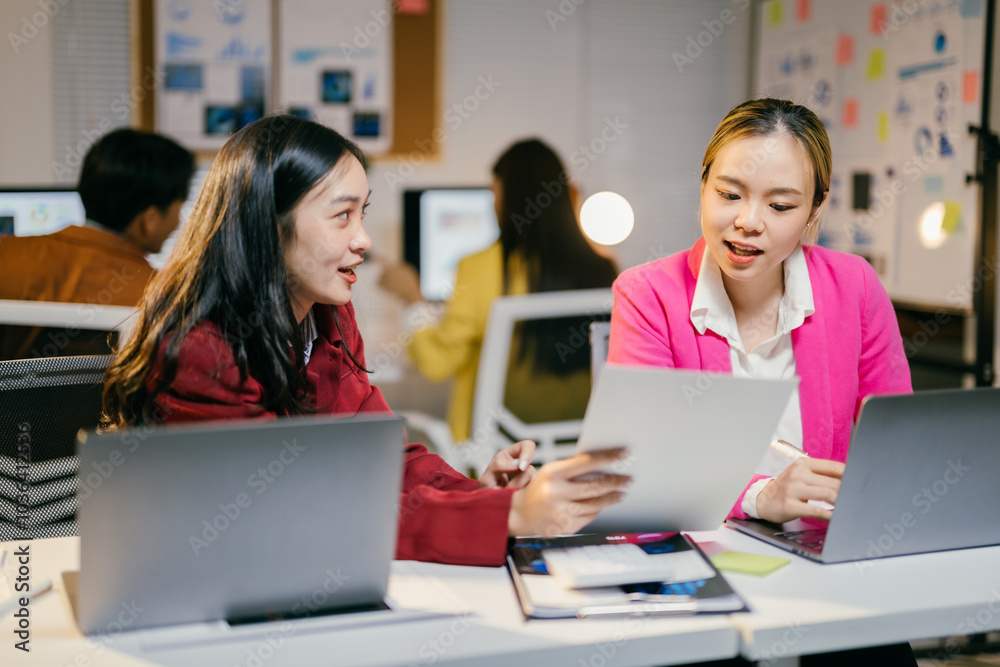 Poster two asian businesswomen are discussing over new project, using laptop computer and analyzing financi