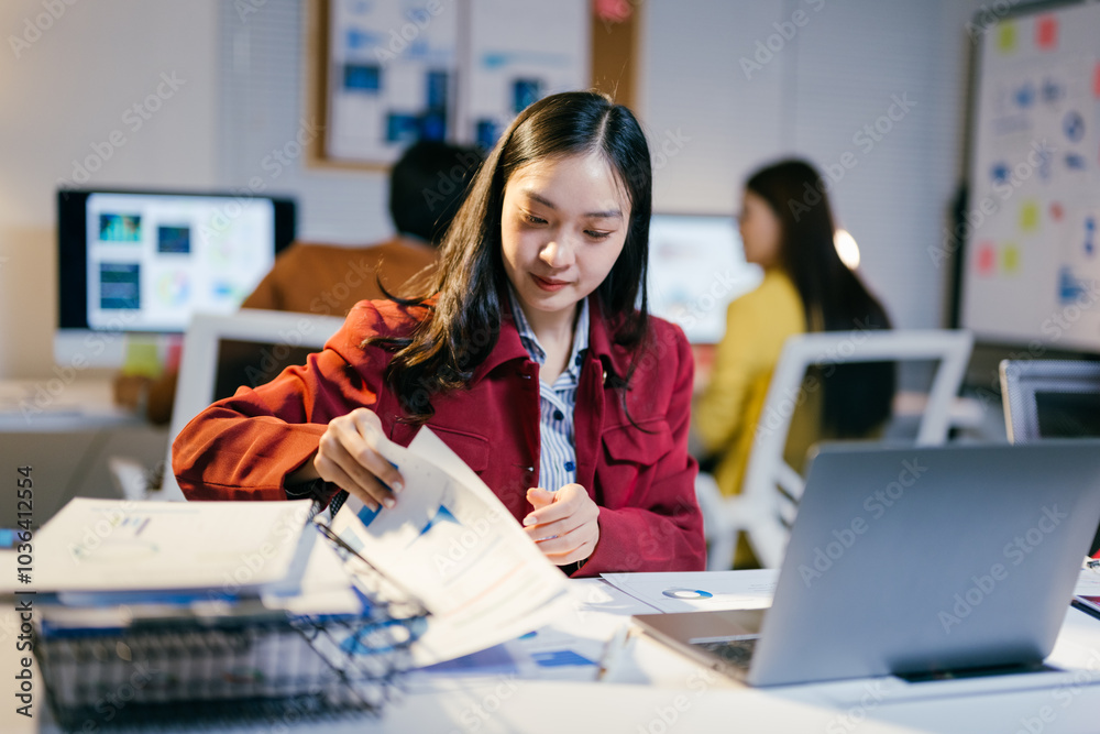 Poster asian businesswoman analyzing financial charts and graphs while working on a laptop computer in a mo