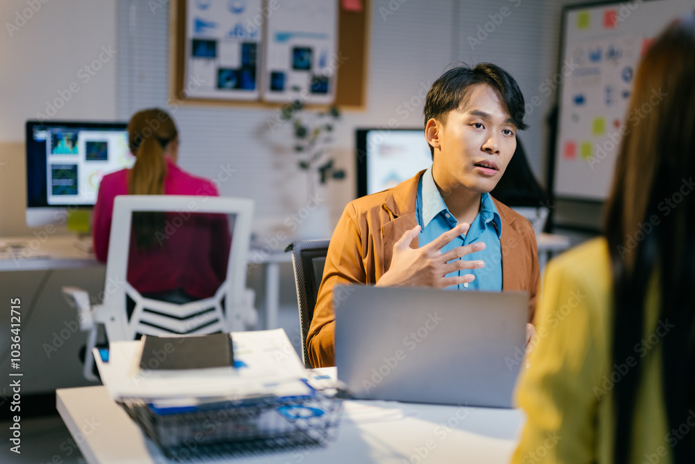 Poster energetic asian manager gestures while discussing work with an employee in a modern office at night,