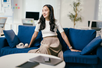 Young asian businesswoman sitting on a blue sofa in a modern office, enjoying a moment of relaxation after a productive day