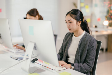 Focused asian businesswoman working on computer in modern office, showcasing dedication and...