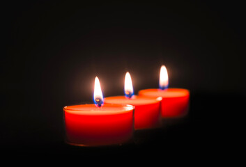 Close-up of three burning candles on black background with copy space on top.
