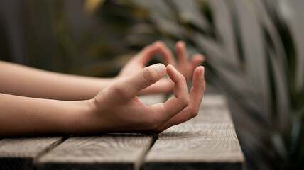 A photo of a pair of hands in a meditative position, with the fingers gently touching each other. The hands are placed on a wooden surface. 