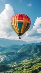 Fototapeta premium Vibrant Hot Air Balloon Drifting Over Lush Mountain Landscape with Scenic Vistas and Serene Clouds