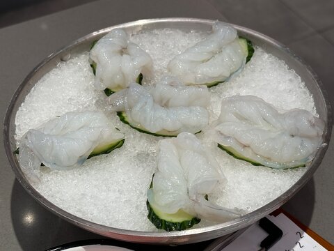 Raw peeled shrimp on crushed ice in a stainless steel bowl, ready for hot pot