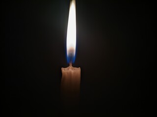 A single unlit candle stands tall against a pitch black background The candle is white with a...