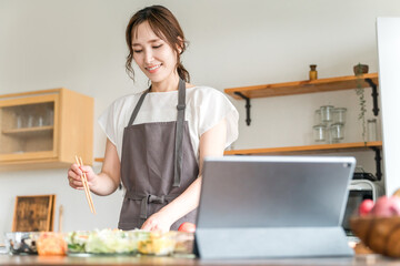 タブレットでアプリを使いレシピを見ながら料理するエプロン姿の女性
