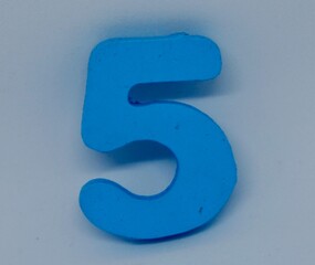 close up photo of a children's toy in the shape of the number five, made of wood painted light blue
