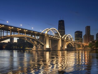 A large, illuminated bridge over a river at night, with a city skyline in the background