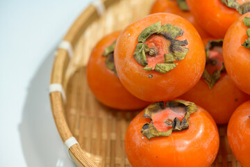 Delicious ripe persimmons in bowl on blurred background, closeup