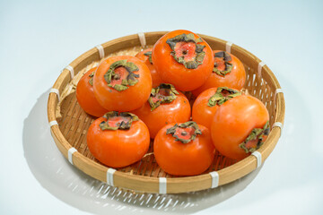 Delicious ripe persimmons in bowl on blurred background, closeup