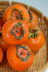 Delicious ripe persimmons in bowl on blurred background, closeup