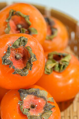 Delicious ripe persimmons in bowl on blurred background, closeup