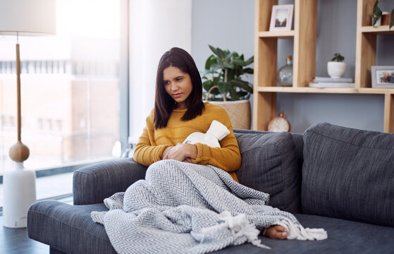 Stomach pain, sickness and woman on sofa with hot water bottle, menstrual cramps and home living room. Comfort, sore abdomen and girl with tummy ache from period, virus or constipation in house - Powered by Adobe