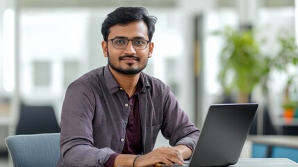 portrait of an Indian software engineer or web developer working on laptop in modern office looking at camera, tech worker