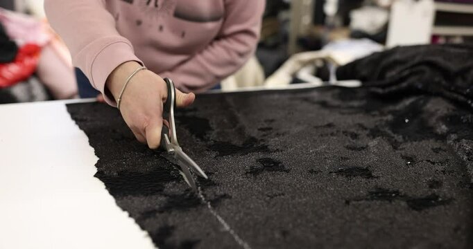 Female tailor carefully cuts fabric using sharp scissors