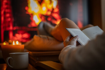 Woman Reads A Book By The Fireplace On A Winter Afternoon. Relaxed Female Dedicates Her Free Time To Reading At Home.
