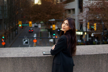 Attractive businesswoman standing against stone railing overlooking a bustling city street filled with traffic lights