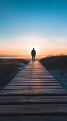 Fototapeta premium Silhouette of a Person Walking on a Wooden Pathway Towards the Ocean