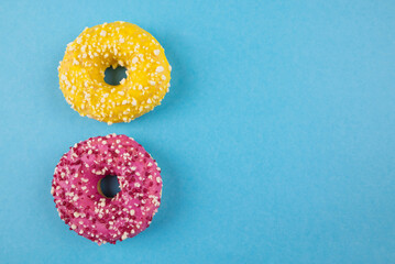Two donuts with colored glaze and sprinkles on blue background with copy space.