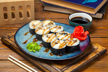 Japanese rolls with red fish and teriyaki sauce on a plate, cafe, restaurant, on a wooden table.