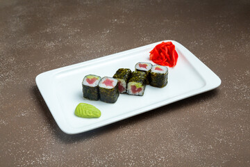 Japanese maki sushi with tuna on a plate with wasadi and ginger on a gray background.