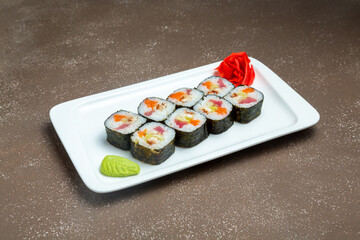 Japanese rolls, sushi with salmon, yun and eel on a plate with wasabi and ginger on a gray background.