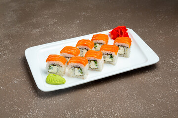 Japanese rolls, California sushi with salmon and cucumber, in sesame on a plate with wasabi and ginger on a gray background.
