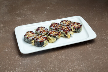 Japanese rolls, sushi fried in breadcrumbs with teriyaki sauce, on a plate on a gray background.