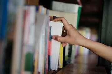 Male hand choosing and picking white book on wooden bookshelf in public library. Education research and self learning in university life concepts