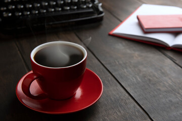 Red cup with hot coffee. Typewriter in background. Concept of business breakfast.