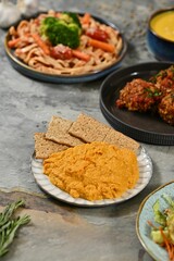 Diverse spread of dishes with hummus and pasta.