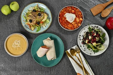 Top view of diverse healthy dishes on a dark surface.