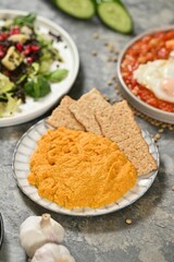 Hummus with crackers and salad on gray surface.