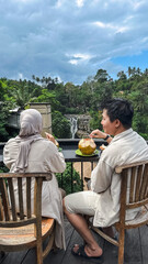 young indonesian couple drinking coconut ice with a waterfall in the background