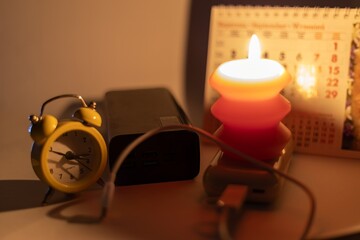 Burning candle and power banks near mechanical clock and calendar. Scheduled power outage due to...
