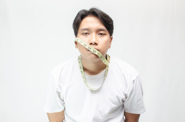 anorexia a diet concept illustrated by young asian man with unhappy expression covering his mouth with a measuring tape. eating disorder concept. extreme diet comcept.