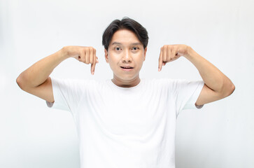 Atrractive young asian man in white t-shirt pointing his finger to advertise something. handsome asian man promoting something and pointing his finger to copy space showing discount or promotion.