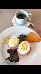 Healthy breakfast of eggs Benedict paired with fresh greens and coffee. Eco-friendly and locally sourced ingredients. Nutritious and sustainable choice for delicious start to day.