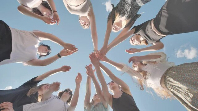 Group of young people is joining hands forming a circle in the sky while smiling.