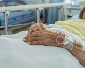 Close up intravenous saline for injection plug in hand of elderly patient lying in the hospital bed...