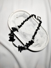 Black irregular beaded gemstone necklace on white gypsum stand close up. Agate jewelry. Bohemian,...