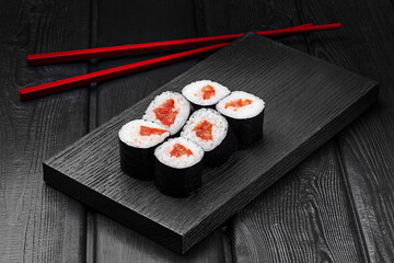 Japanese rolls, maki sushi with tomato on black wooden background.