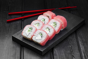 Japanese rolls, Philadelphia sushi with tuna, cucumber and cheese on a black wooden background.