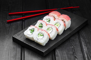 Japanese rolls, Philadelphia sushi with tuna, cucumber and cheese on a black wooden background.