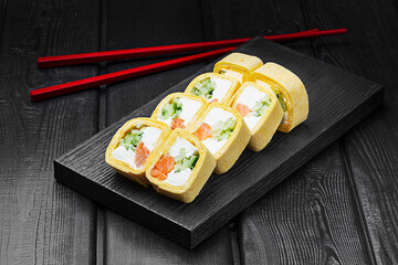 Japanese rolls, sushi in tortilla with salmon, cucumber and cream cheese on black wooden background.
