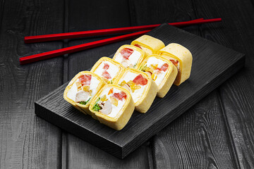 Japanese rolls, sushi in tortilla with chicken, pepper and tomato and cream cheese on black wooden background.