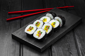Japanese rolls, sushi with pepper, tomato, cucumber and cheese on a black wooden background.